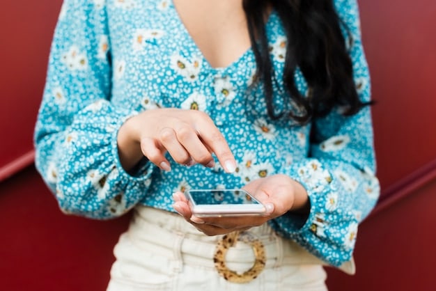 Close-up of a person's hands scrolling through a fashion blog on a smartphone, focusing on an article discussing upcoming fashion drops. The screen highlights specific dates and brands.