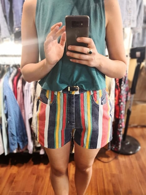 A person using a smartphone to browse a fashion resale app. The app displays images of various trendy clothing items and accessories with their current resale prices.